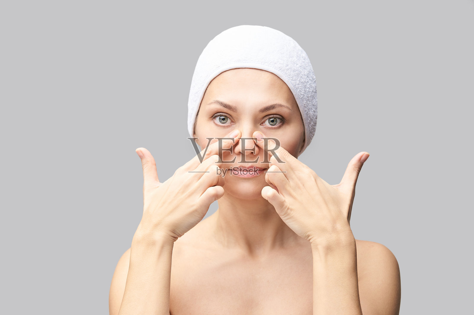 漂亮女人给自己做面部按摩。灰色背景。照片摄影图片