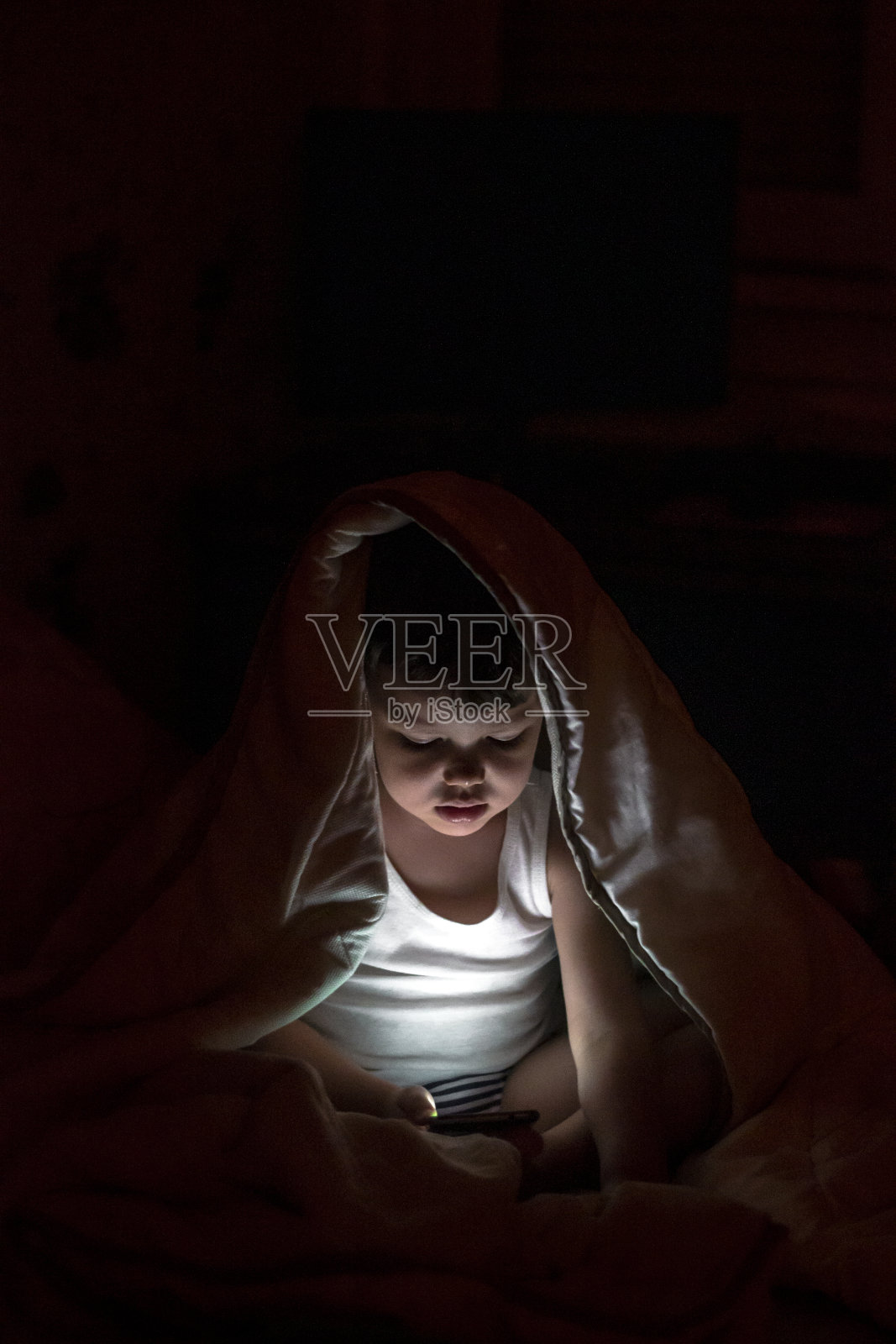 蹒跚学步的孩子，脸被手机屏幕照亮。照片摄影图片