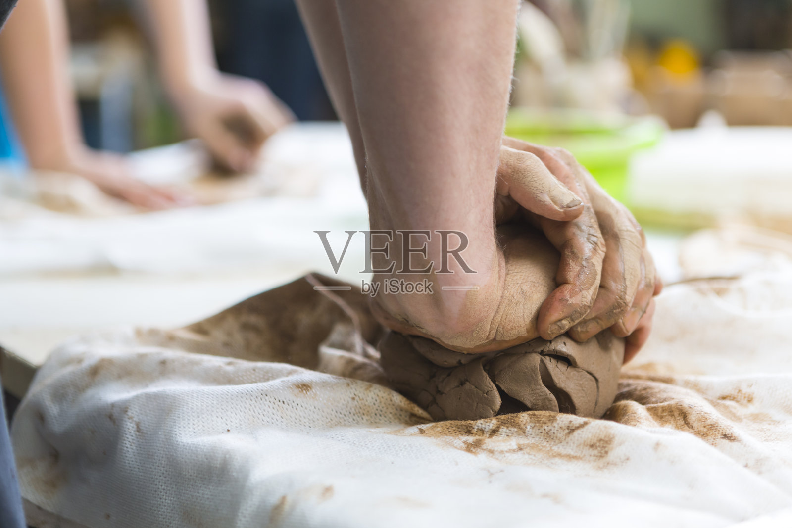 漫步的概念。男工人的手在围裙滚动一块湿粘土在成型前的桌子上的特写。水平射照片摄影图片