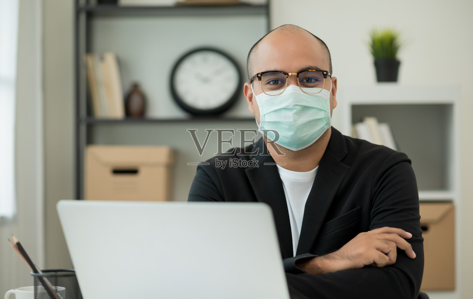 年轻的商人戴着防护面具在办公室用笔记本电脑工作。社交距离安全与冠状病毒流感。照片摄影图片