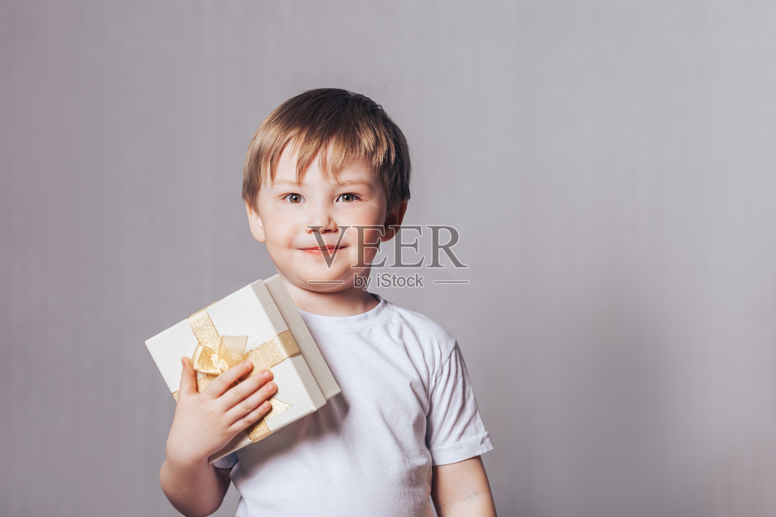 穿着白色t恤的漂亮小男孩手里拿着一份礼物照片摄影图片