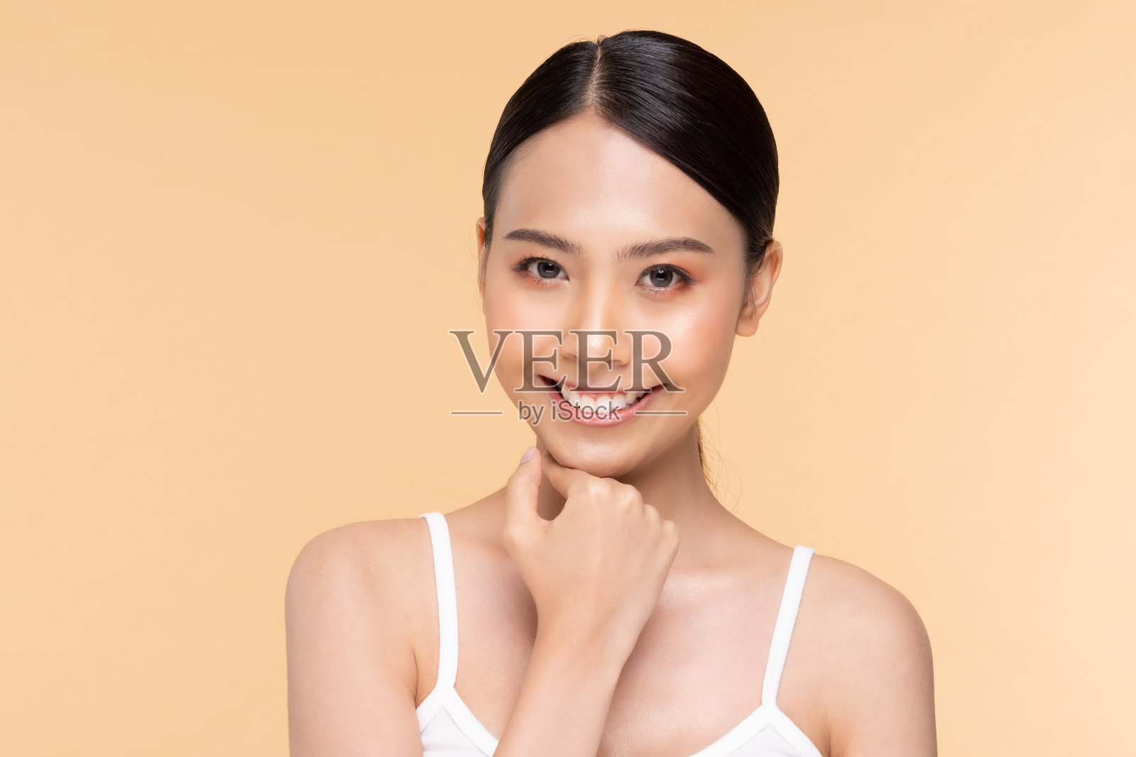 美丽的亚洲女人触摸下巴微笑，干净和新鲜的皮肤，幸福和愉快的情绪积极，米色背景，美容化妆品和水疗护理的概念照片摄影图片