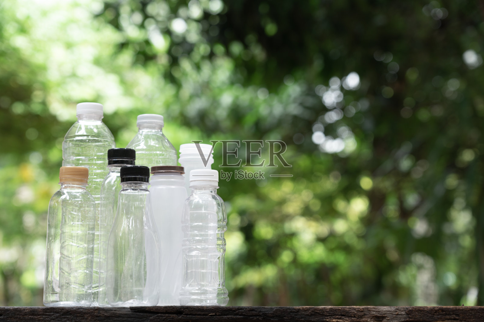 许多不同形状的饮料瓶排列成模糊的绿色花园背景，再利用容器，生态友好的概念，复制空间照片摄影图片