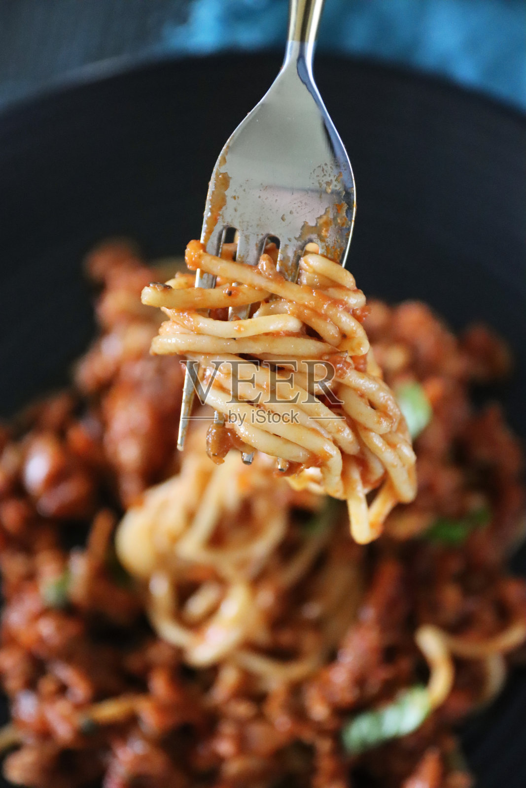 这是一个旋转的金属叉子，上面撒着自制的瘦牛肉碎肉酱、浓郁的番茄酱、洋葱、大蒜和罗勒叶装饰的意大利面，黑色的盘子上放着一部分，俯瞰风景照片摄影图片