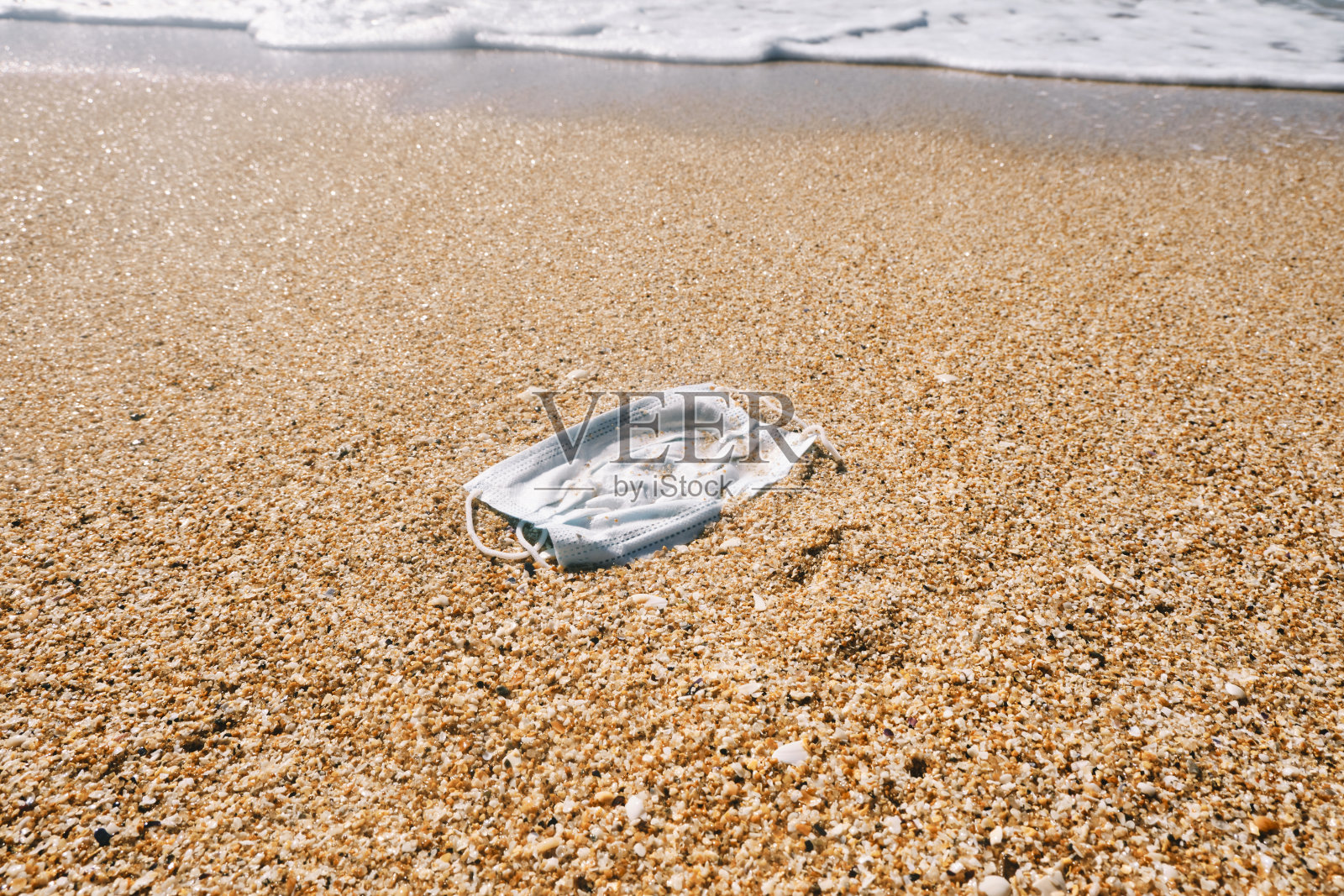 在阳光明媚的海滩上，被冲上岸的一次性冠状病毒面膜。照片摄影图片