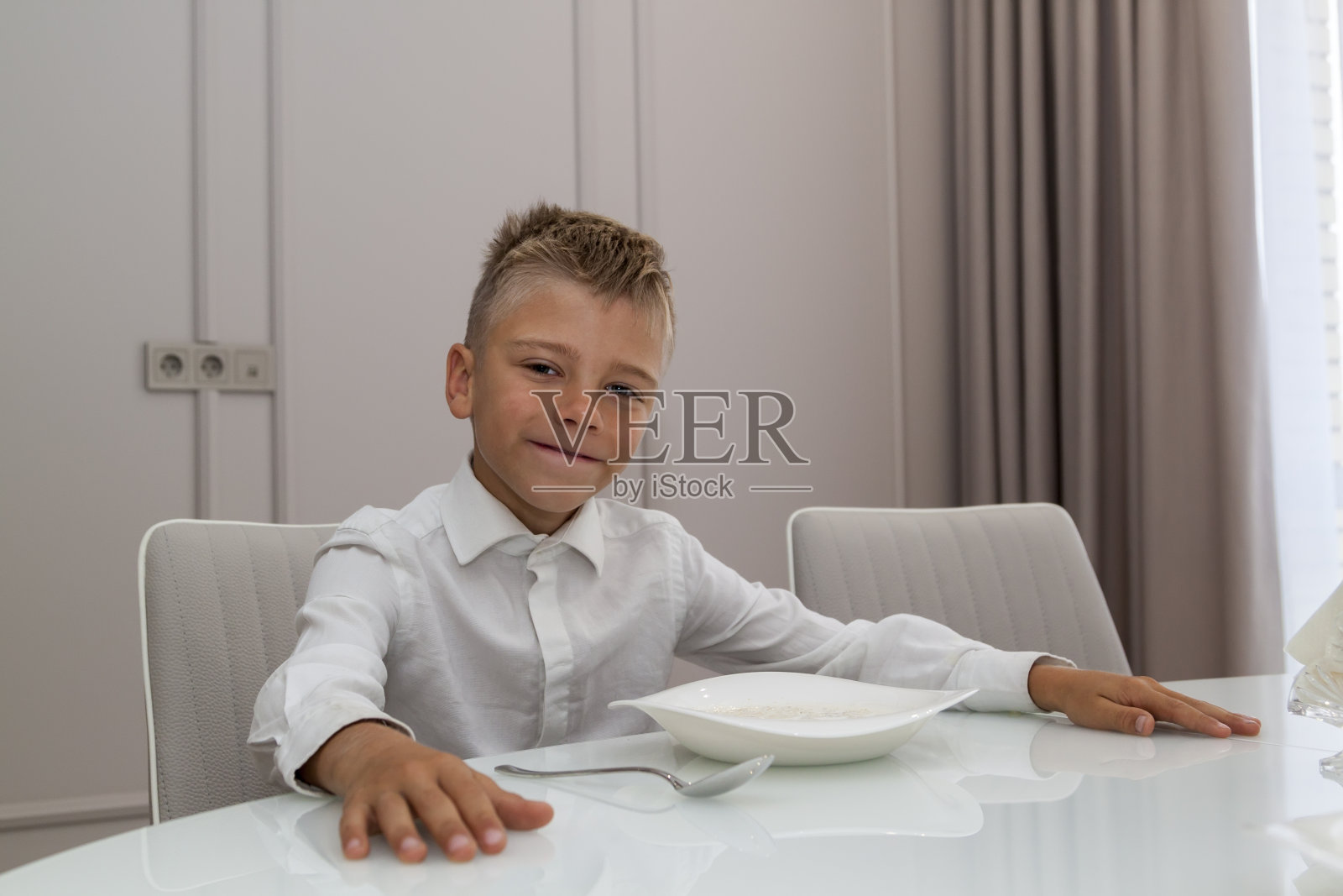 孩子们在宽敞明亮的餐厅的玻璃餐桌上吃午餐，全景窗户。男孩上学前吃粥照片摄影图片