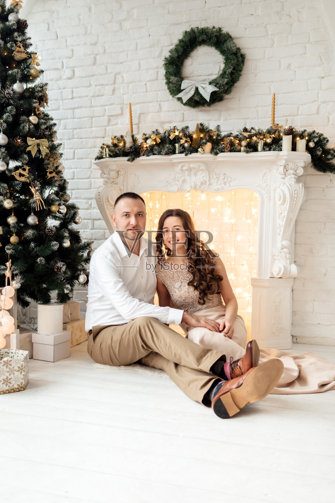 圣诞快乐。年轻夫妇在壁炉附近庆祝圣诞节。幸福的年轻夫妇坐在家里的圣诞树旁。年轻夫妇在圣诞节期间拥抱的照片照片摄影图片