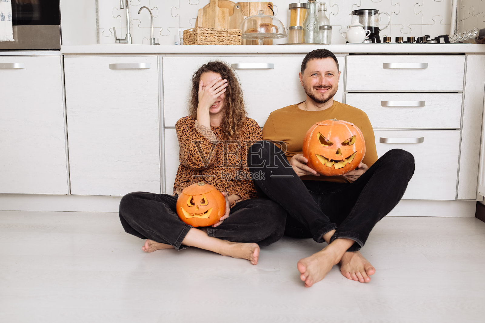 年轻夫妇男女坐在家里厨房的地板上玩，准备万圣节，谈笑风生照片摄影图片