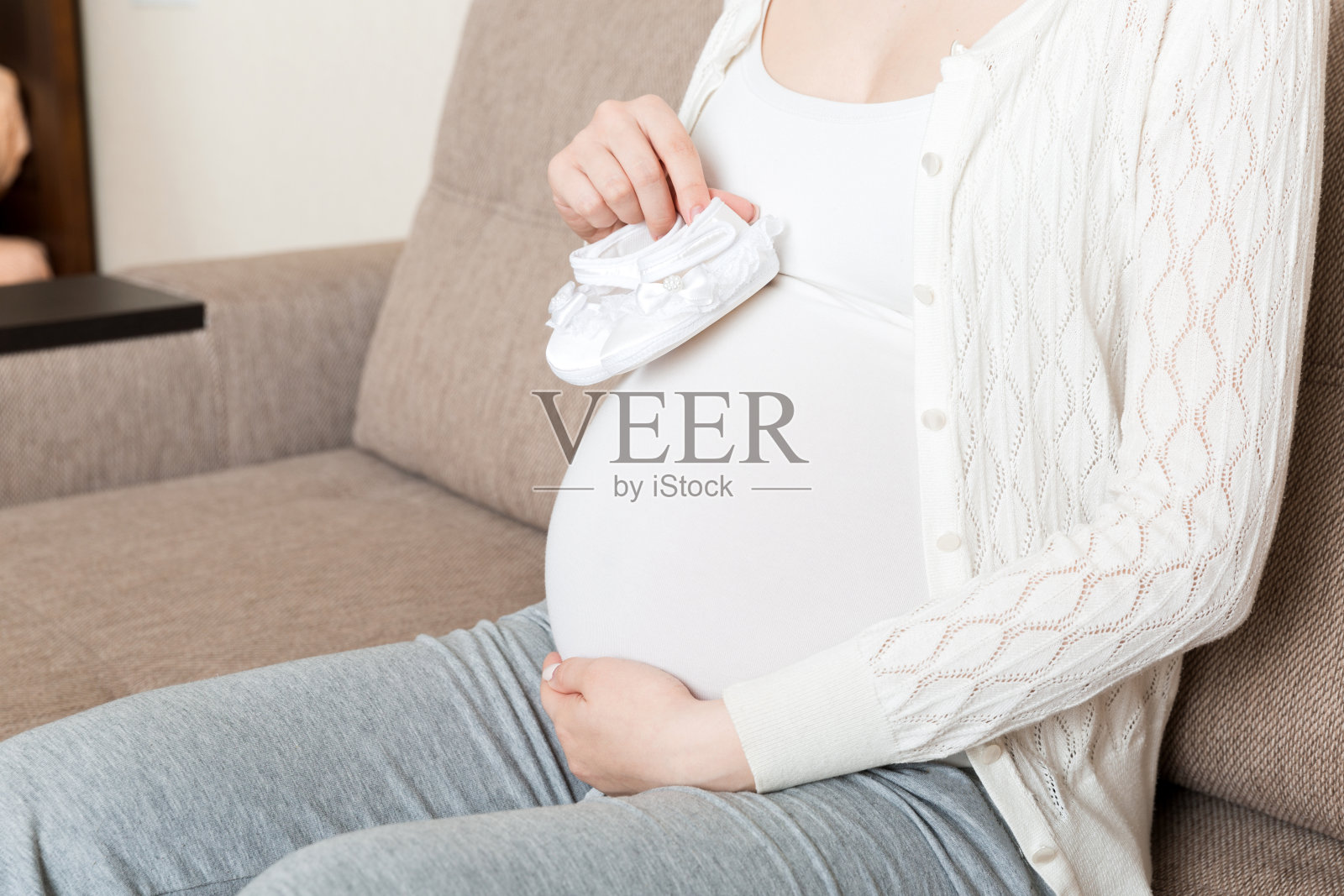 孕妇在家里沙发上为肚子里未出生的婴儿准备的小鞋子照片摄影图片