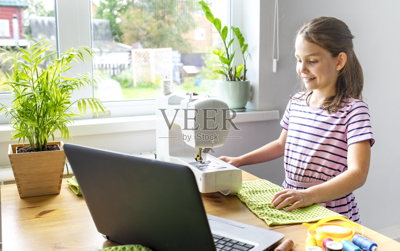 远程教育的概念。Covid封锁。一个十几岁的白人女孩在自我隔离期间学会了在线缝纫。有选择性的重点照片摄影图片