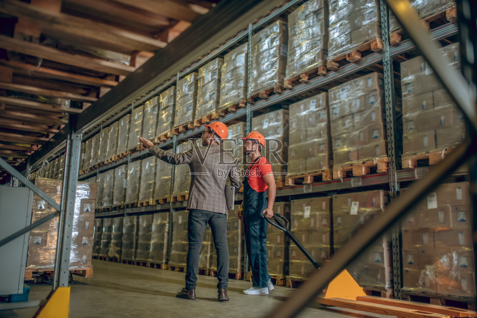 戴着橙色头盔的经理与仓库工人交谈，并向他展示集装箱照片摄影图片