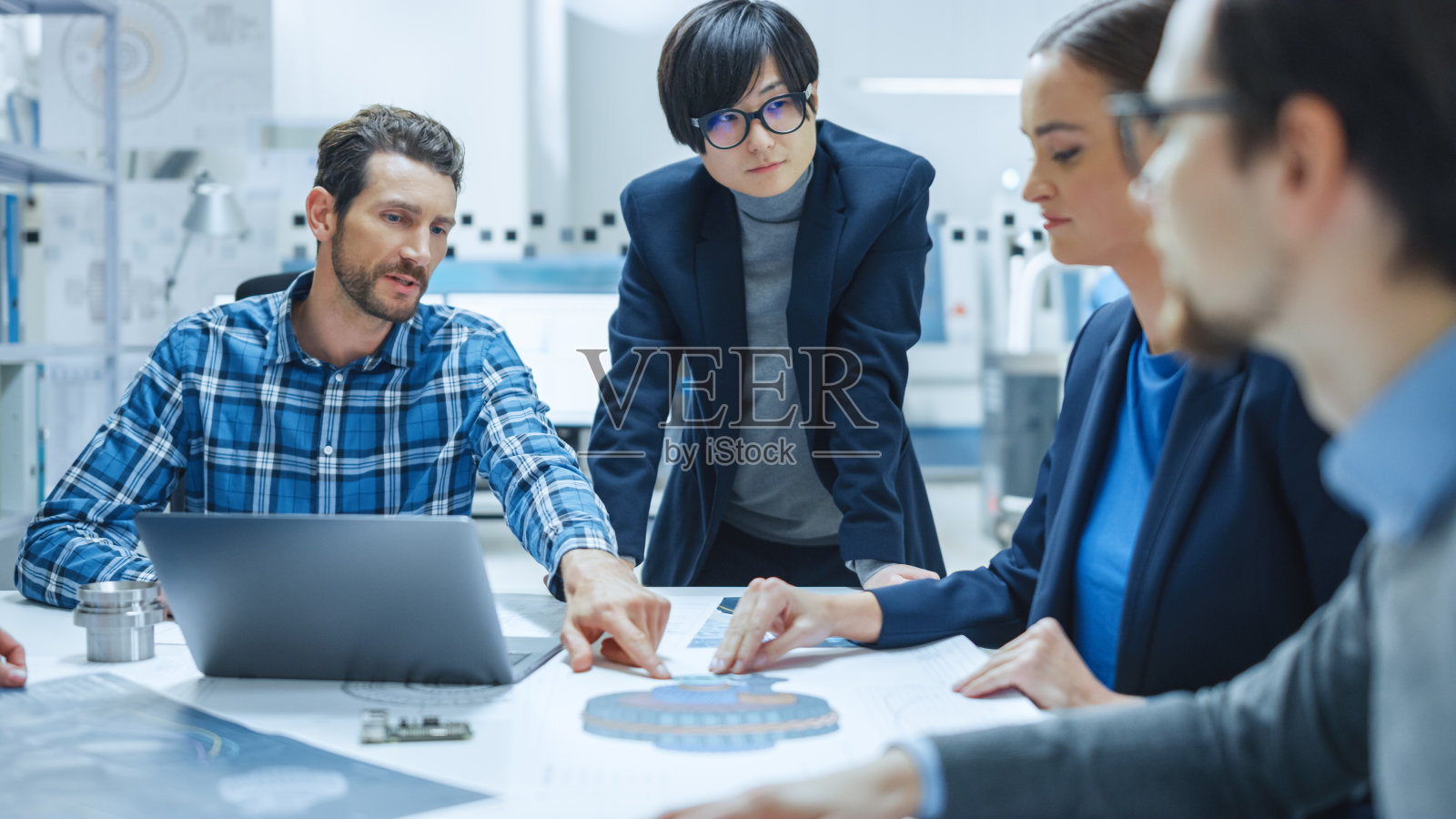 现代工厂办公室会议室:年轻女性专家向坐在会议桌上分析蓝图的工程师、经理、商人和投资者团队报告照片摄影图片