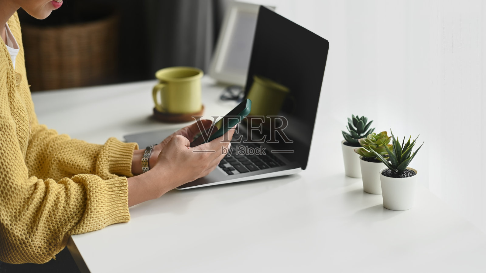 年轻女性自由职业者在她的工作空间使用智能手机和笔记本电脑的剪影。照片摄影图片