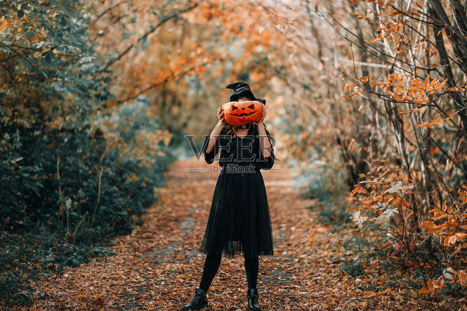 女人在万圣节女巫服装拿着一个大南瓜雕刻的脸照片摄影图片