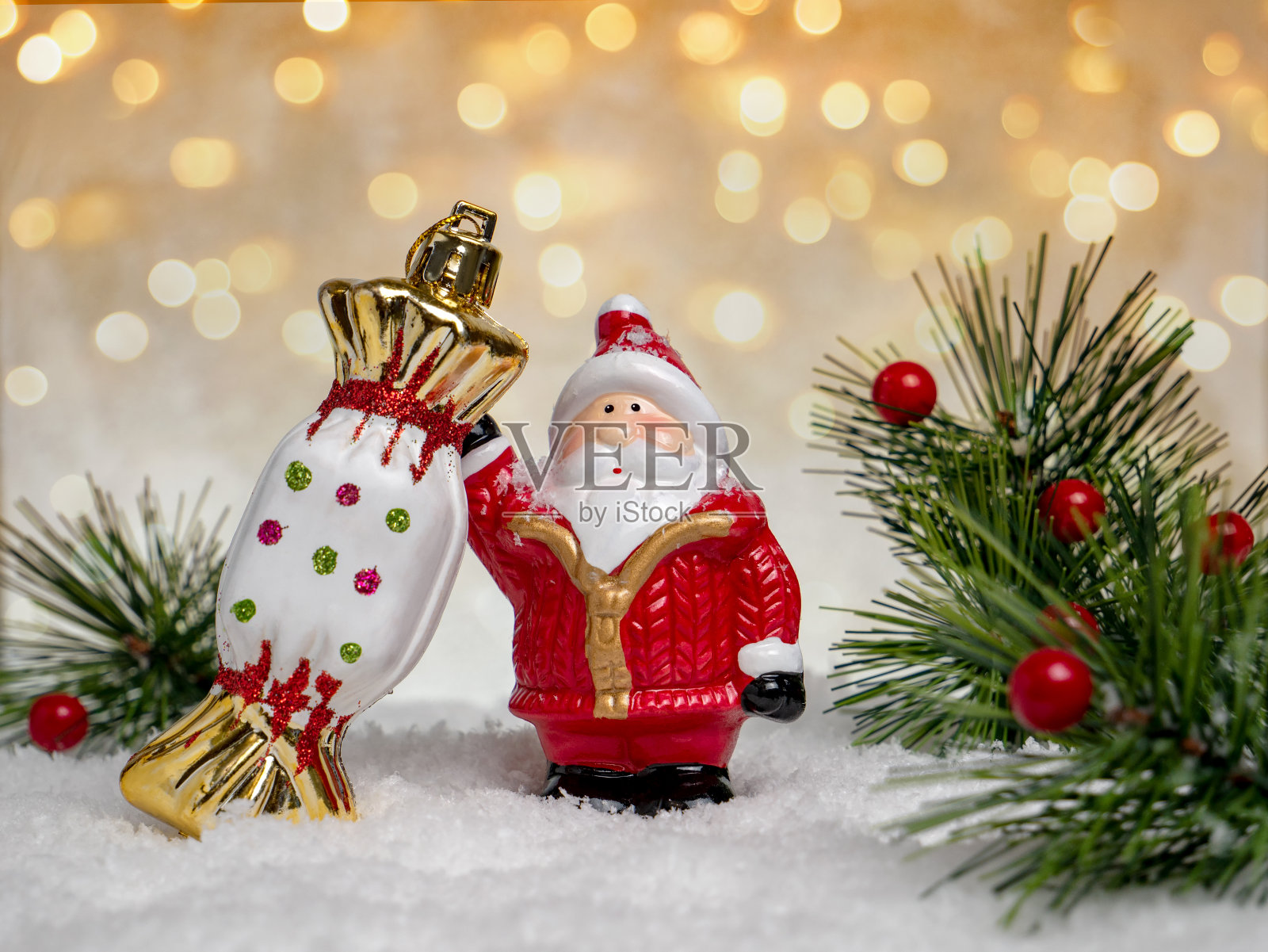 有趣的玩具圣诞老人与糖果在冬天的雪背景与彩色的散焦和冷杉树枝。圣诞节或冬季照片摄影图片