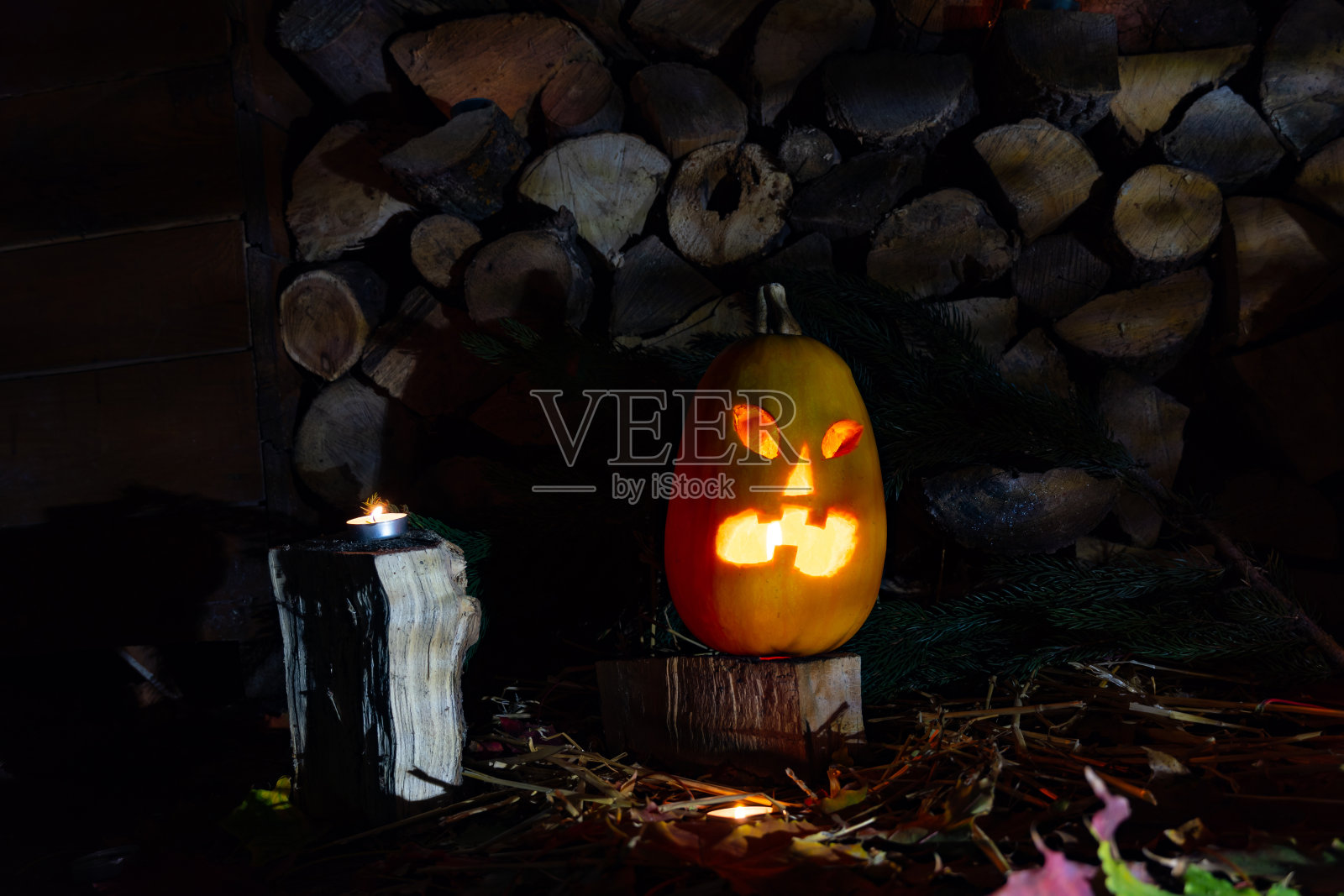 在万圣节的夜晚，发光的南瓜与蜡烛在柴火和秋天的树叶的背景。照片摄影图片