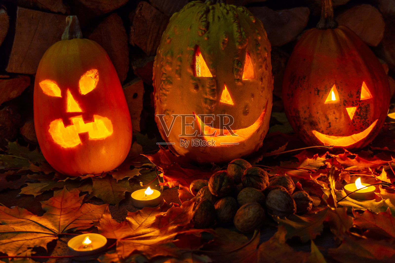 在万圣节之夜，三个发光的南瓜和蜡烛，背景是柴火和秋天的树叶。照片摄影图片