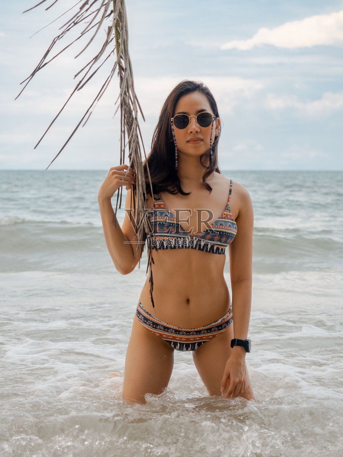 性感的亚洲女人在比基尼姿势与椰子叶在古岛的热带海滩，泰国。暑假的概念。照片摄影图片