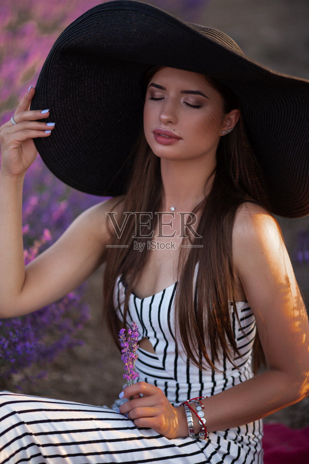 漂亮的女孩戴着大帽子坐在薰衣草田，法国。照片摄影图片