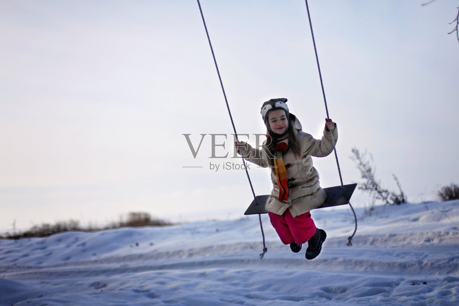 微笑的学龄前女孩在冬天的秋千上飞翔照片摄影图片