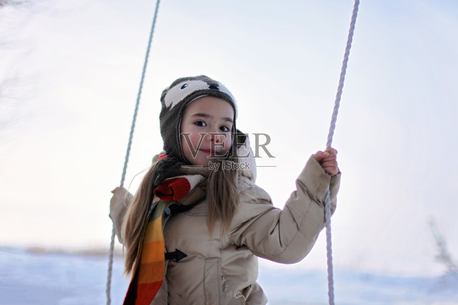微笑的学龄前女孩在冬天的秋千上飞翔照片摄影图片