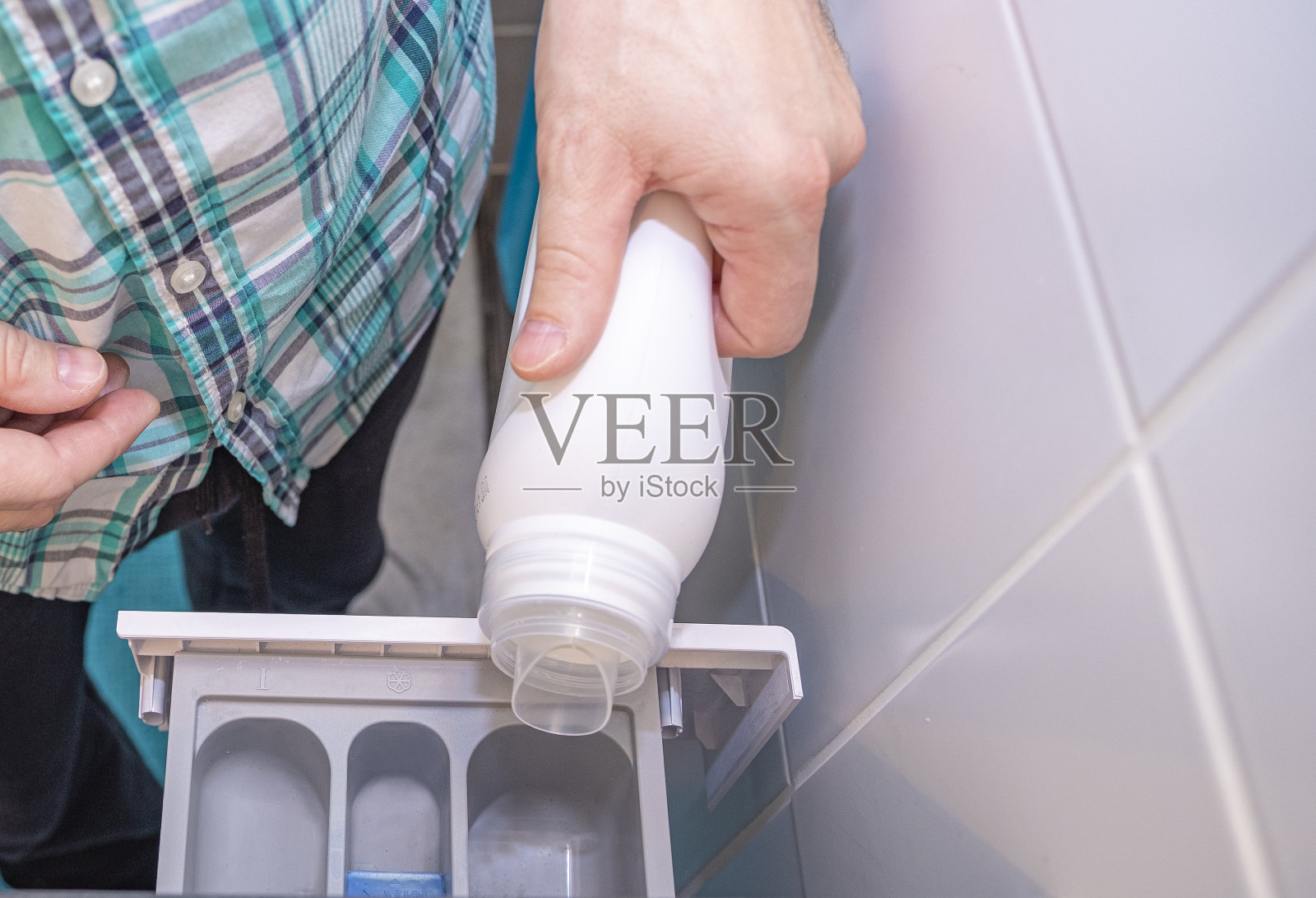 男人的手和洗衣机。一个男人倒了一剂织物柔软剂或漂白剂。特写镜头。照片摄影图片