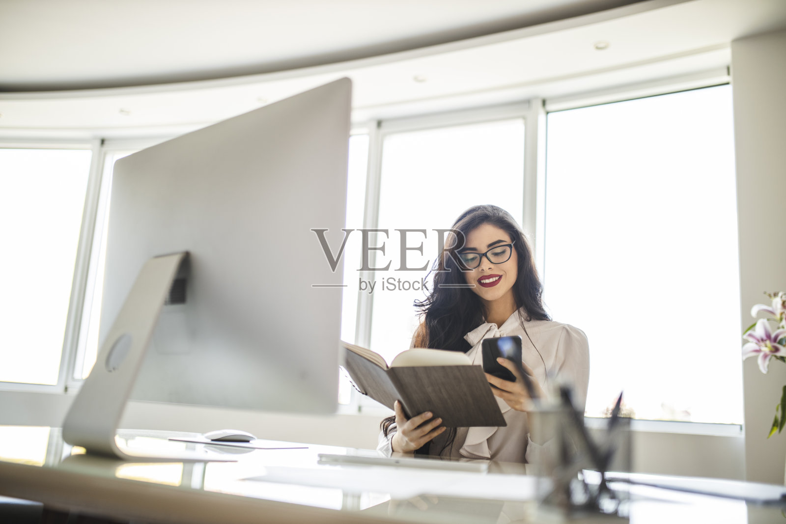 美丽的年轻女子使用她的智能手机，阅读文件和工作在她的办公室照片摄影图片