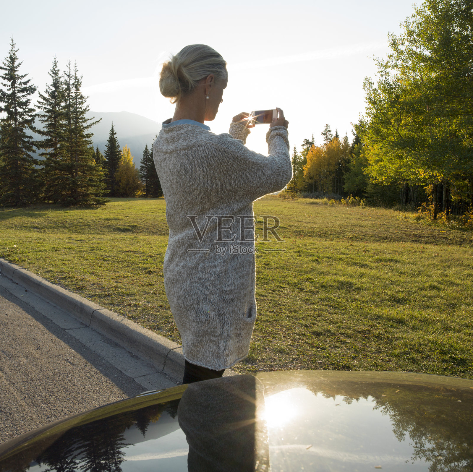 日出时分，妇女倚在停在乡村公路上的汽车上照片摄影图片