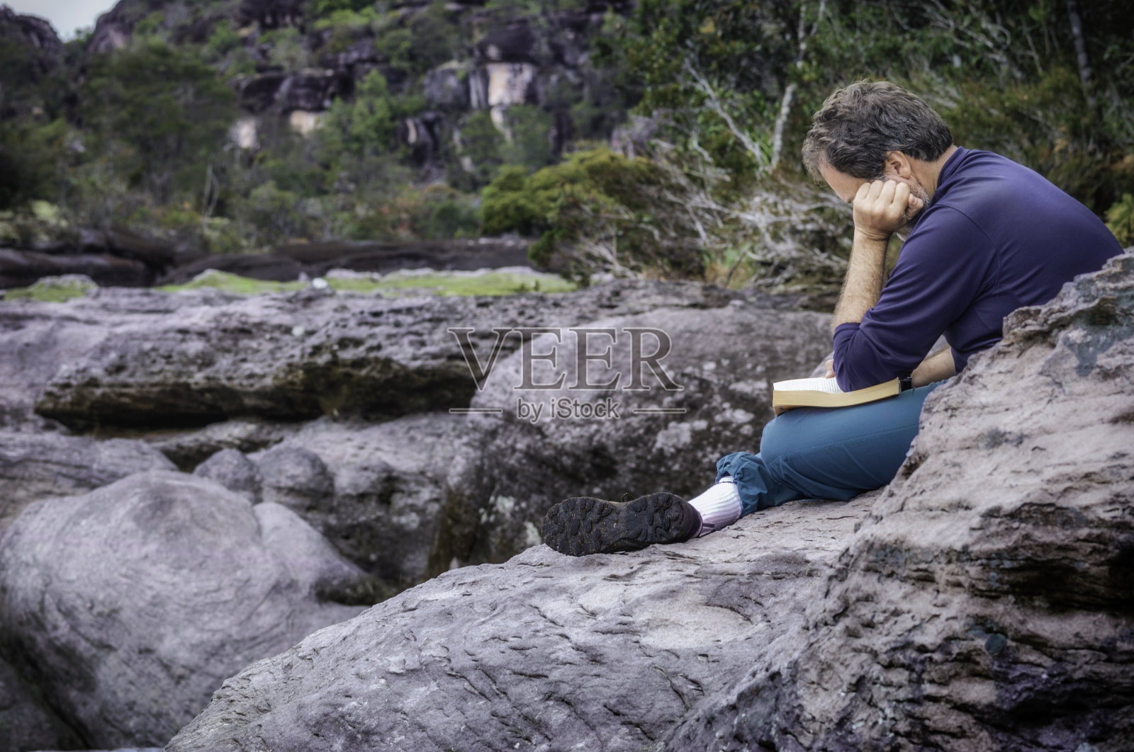 一个成熟的人在探险途中在岩石上看书照片摄影图片
