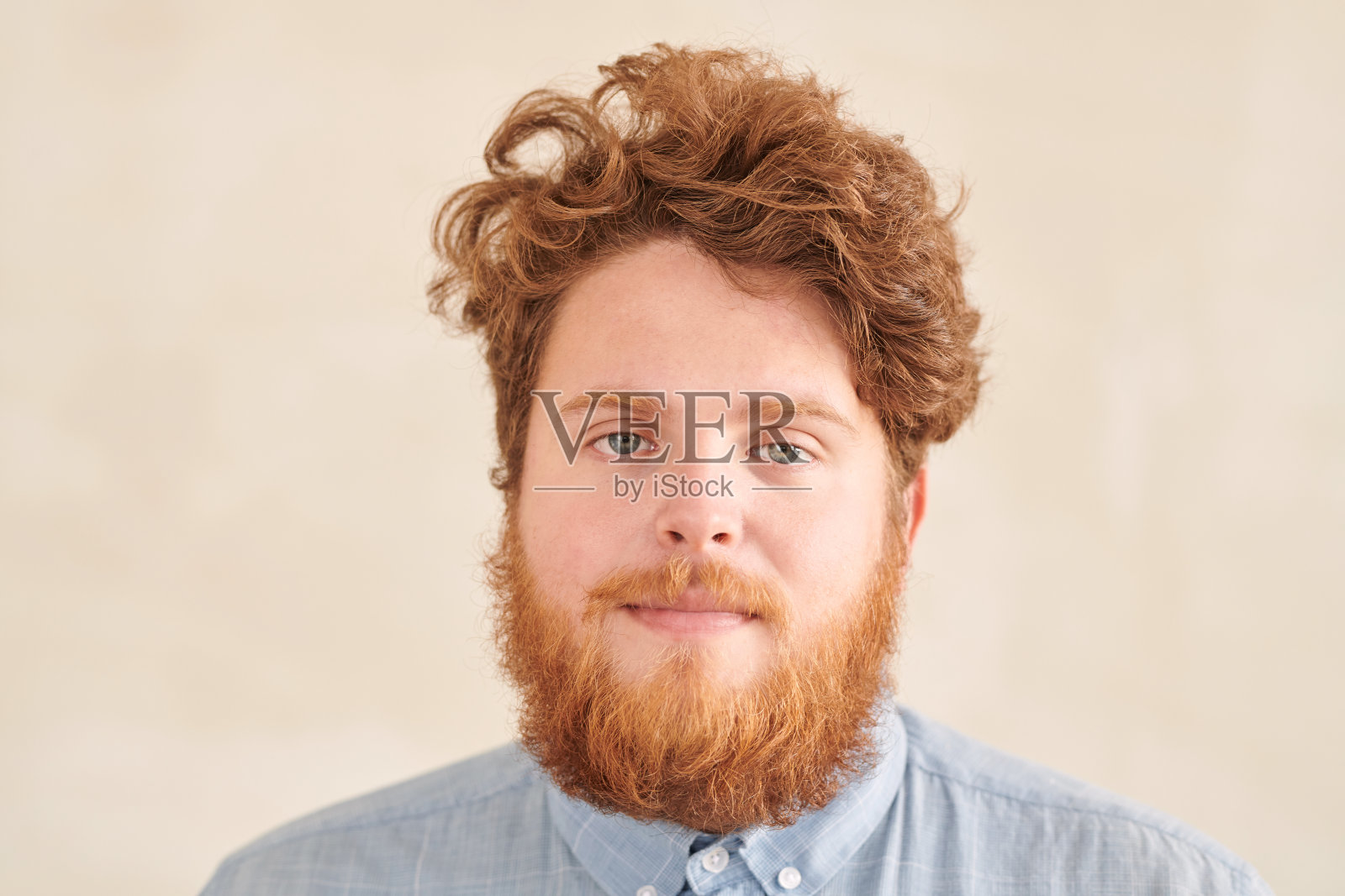 严肃的红发年轻学生的肖像与胡子和小胡子卷发站在米色背景照片摄影图片