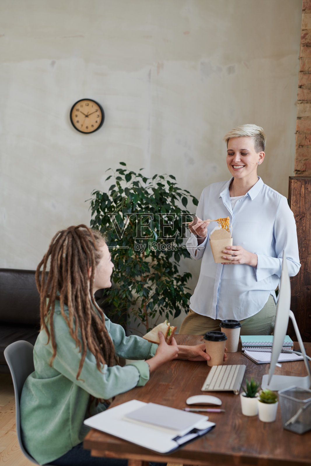快乐的年轻女性在工作场所吃零食，在现代办公室讨论网页设计照片摄影图片