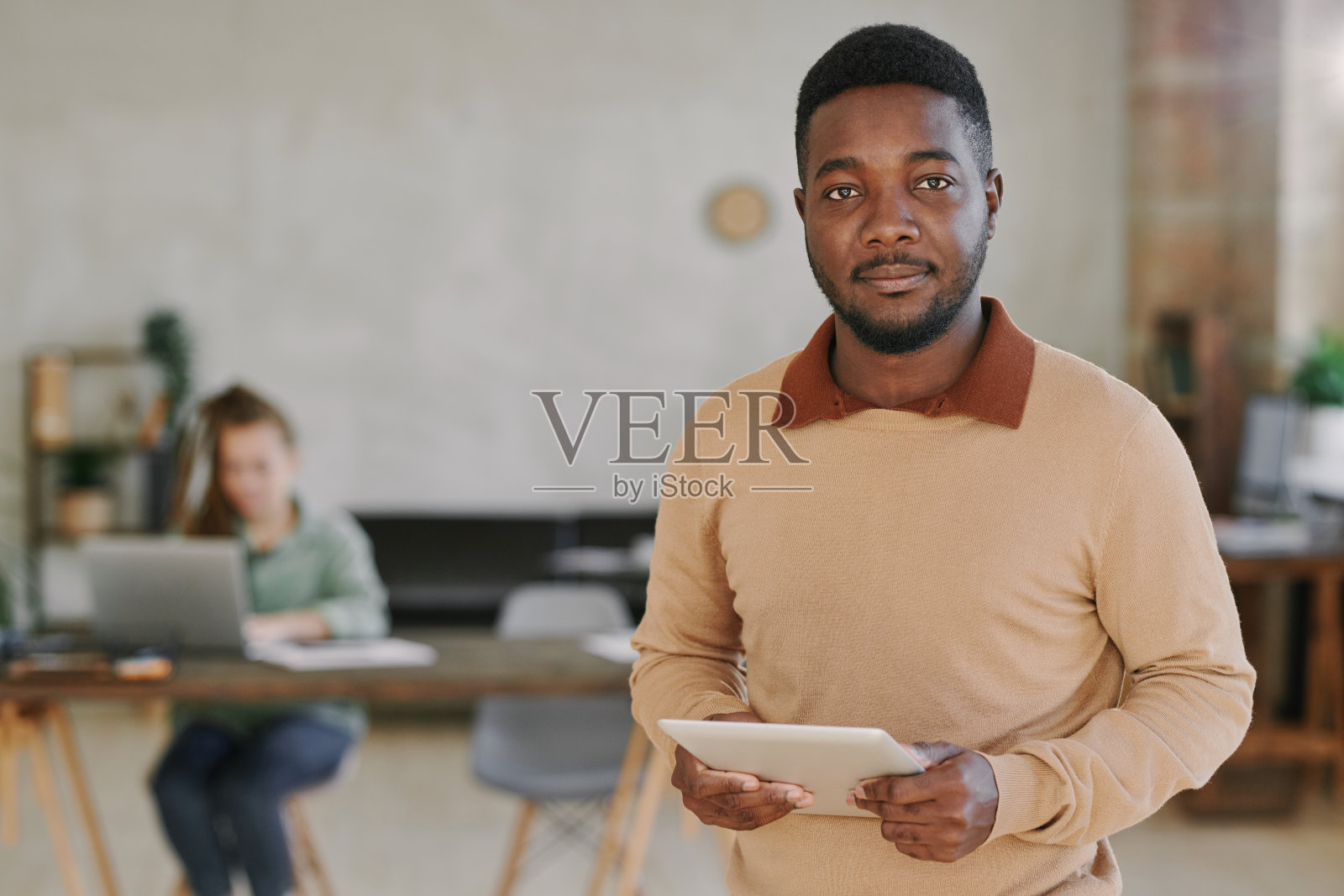 一幅严肃英俊的年轻非裔美国员工的肖像，穿着米色毛衣，站在办公室里的数字平板电脑前照片摄影图片