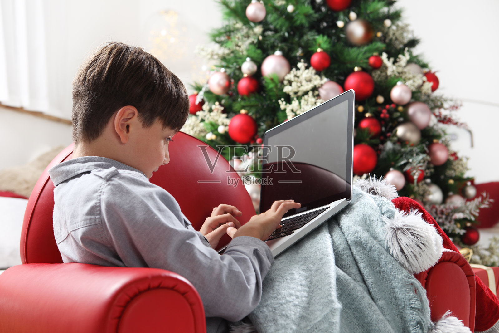 圣诞快乐，孩子在家中电脑旁，靠近灯光装饰的圣诞树照片摄影图片