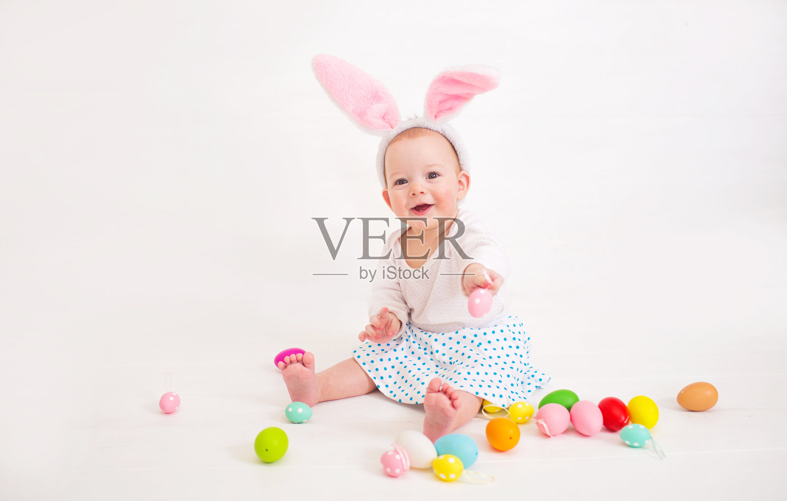 一个穿着复活节兔子服装的孩子坐在白色背景的地板上玩耍照片摄影图片