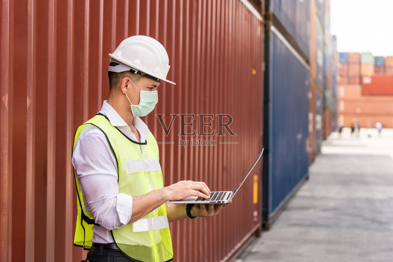 肖像工作者使用笔记本电脑，戴着外科口罩和安全白头，以保护工作场所的污染和病毒在担心冠状病毒大流行照片摄影图片