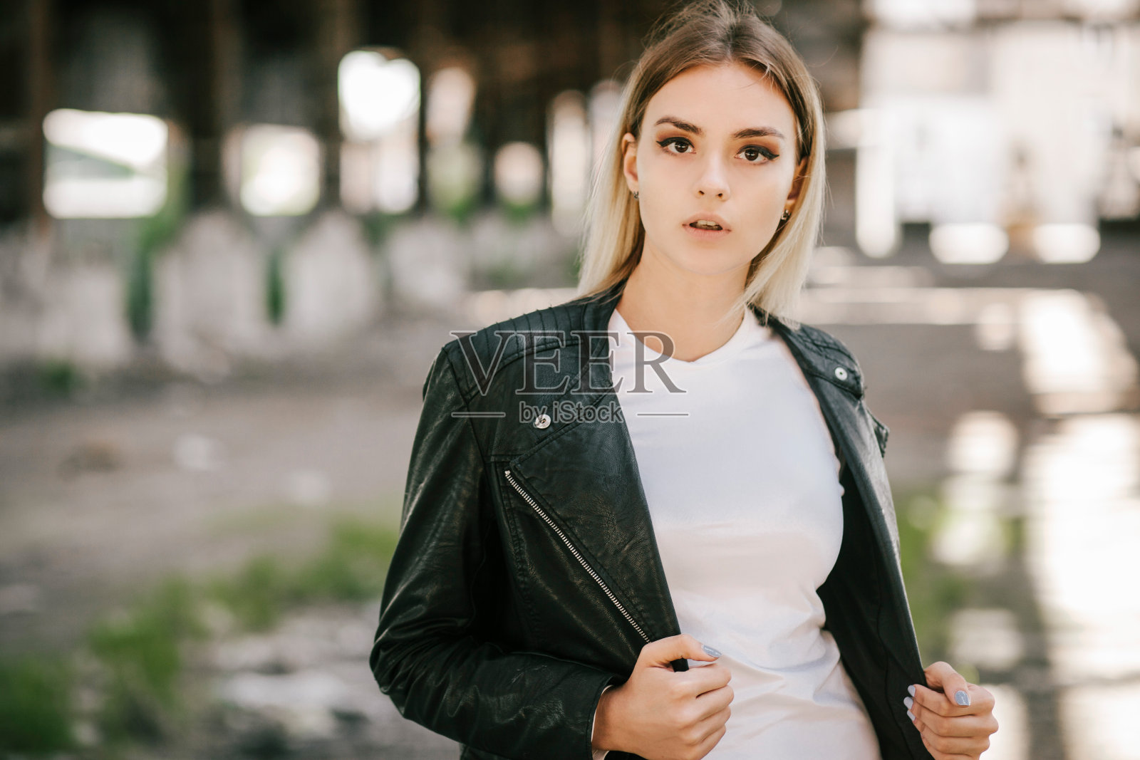 女孩穿着t恤，眼镜和皮夹克摆姿势，街头，城市的服装风格。街头摄影照片摄影图片