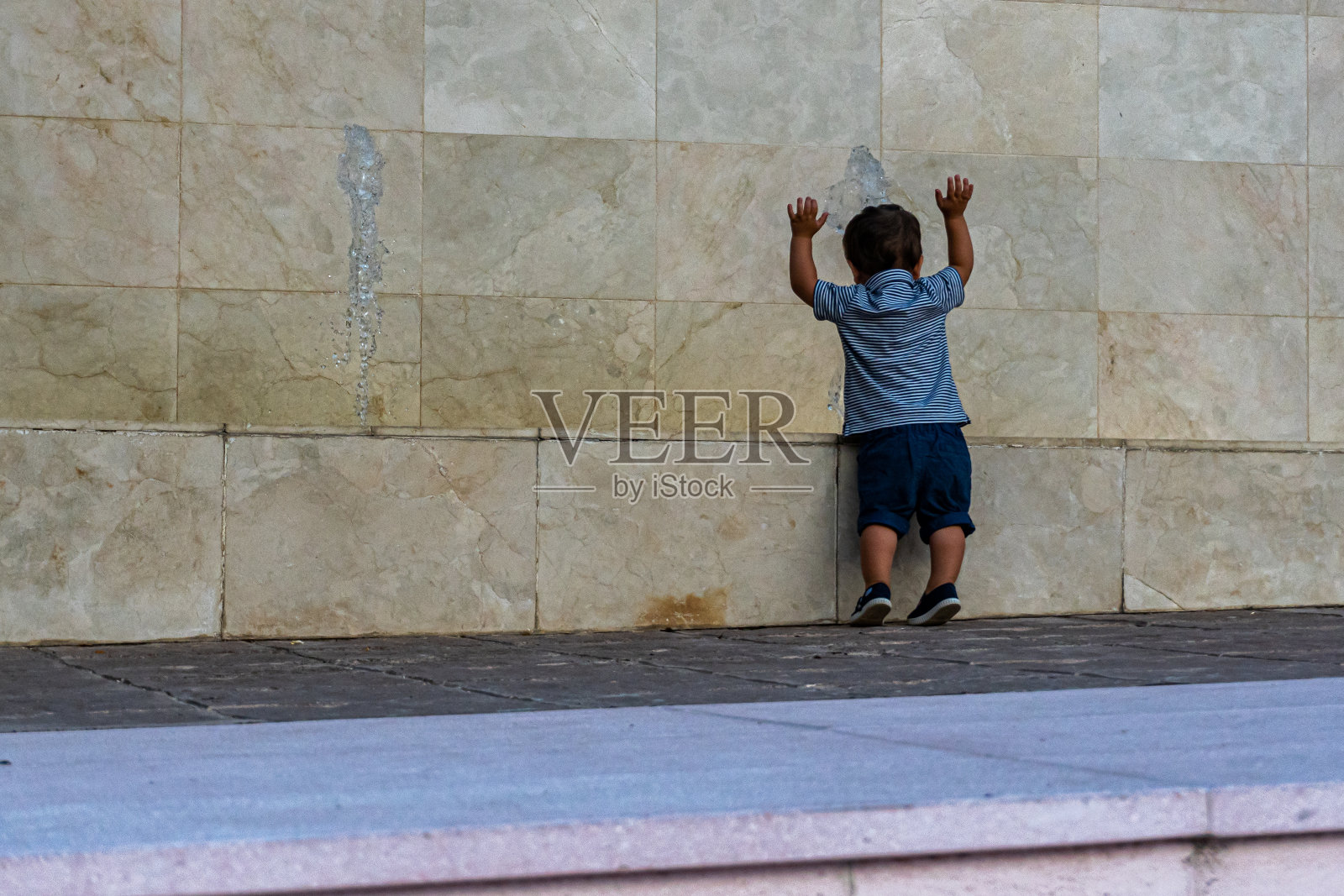 一个孩子穿着蓝色短裤，背对着一个蜷伏的大理石栏杆照片摄影图片