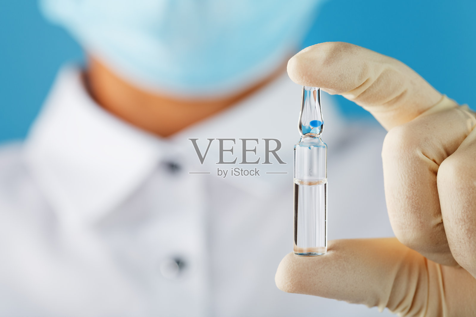 安瓿中含有对抗疾病病毒的疫苗在蓝色背景下放在医生、科学家手中，戴着手套和口罩。照片摄影图片