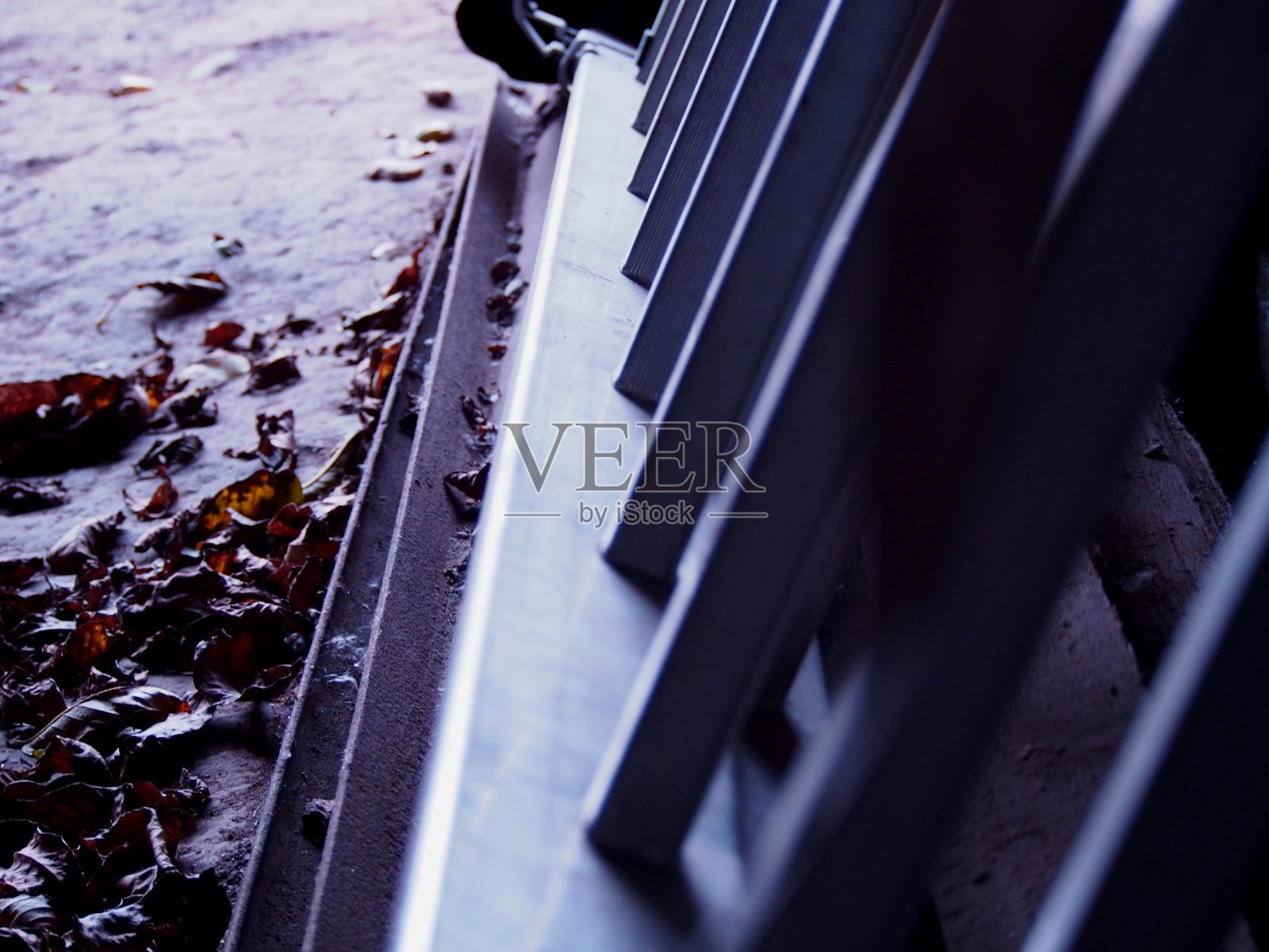 银色的铝梯躺在泥土地上，上面是秋天的枯叶，阴郁的心情，褐色的背景，照片摄影图片