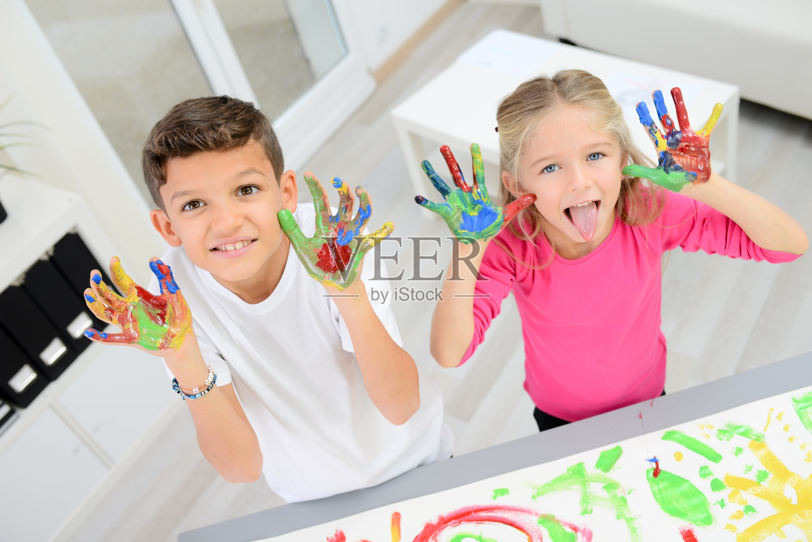 两个漂亮的小男孩和女孩用彩色颜料在白纸上手绘照片摄影图片