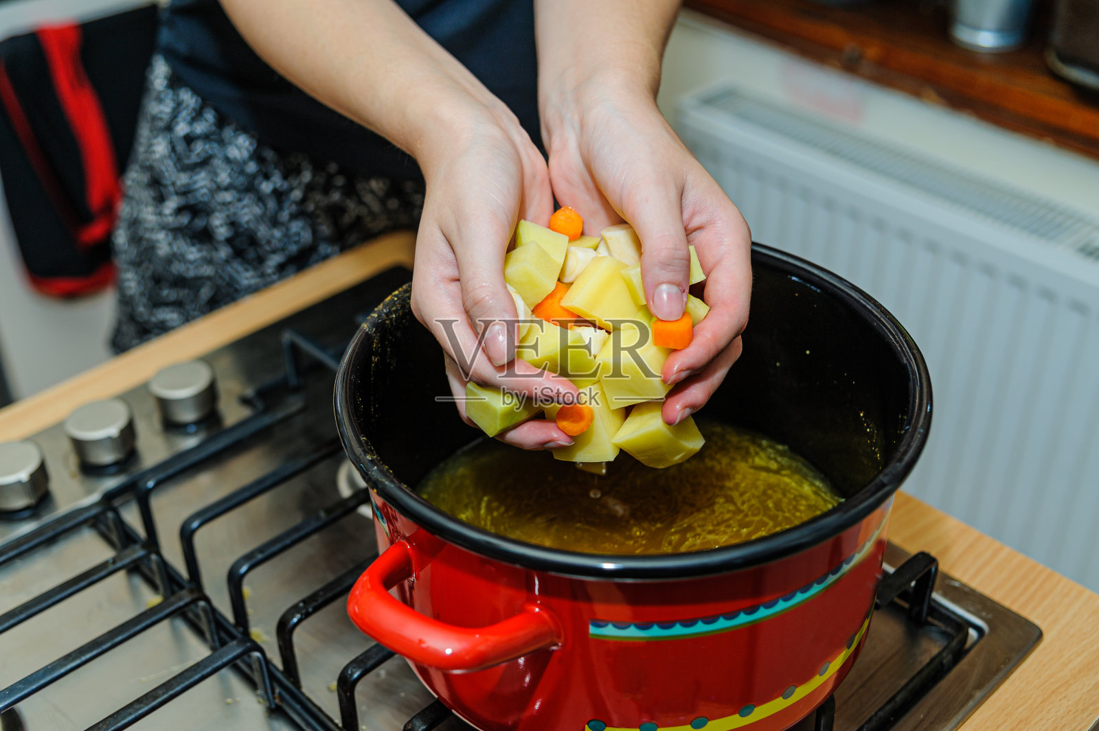 一位女厨师正在为她正在做的美味汤添加新鲜的蔬菜。照片摄影图片