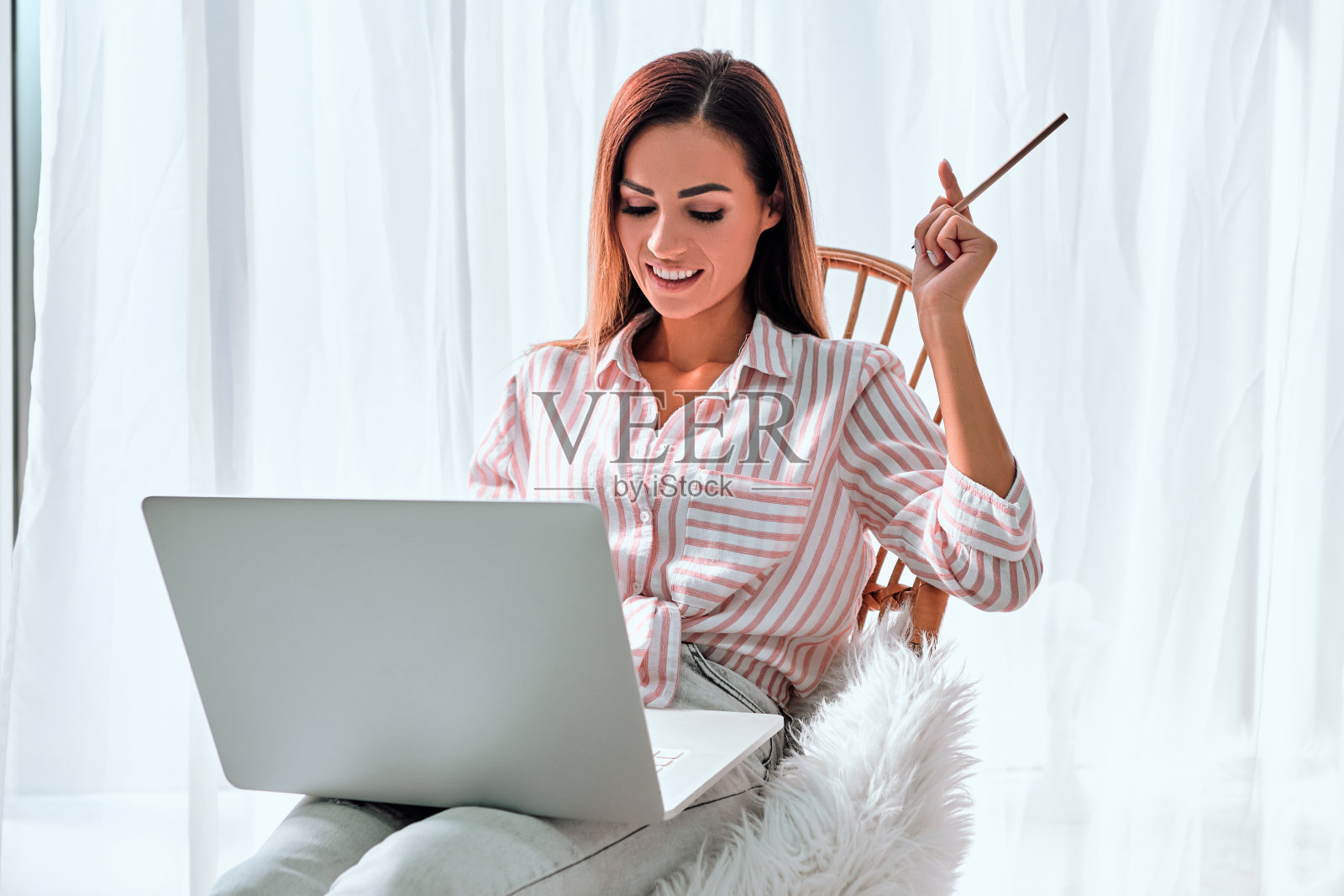 微笑的年轻女企业家坐在她家庭办公室的扶手椅上用笔记本电脑工作照片摄影图片