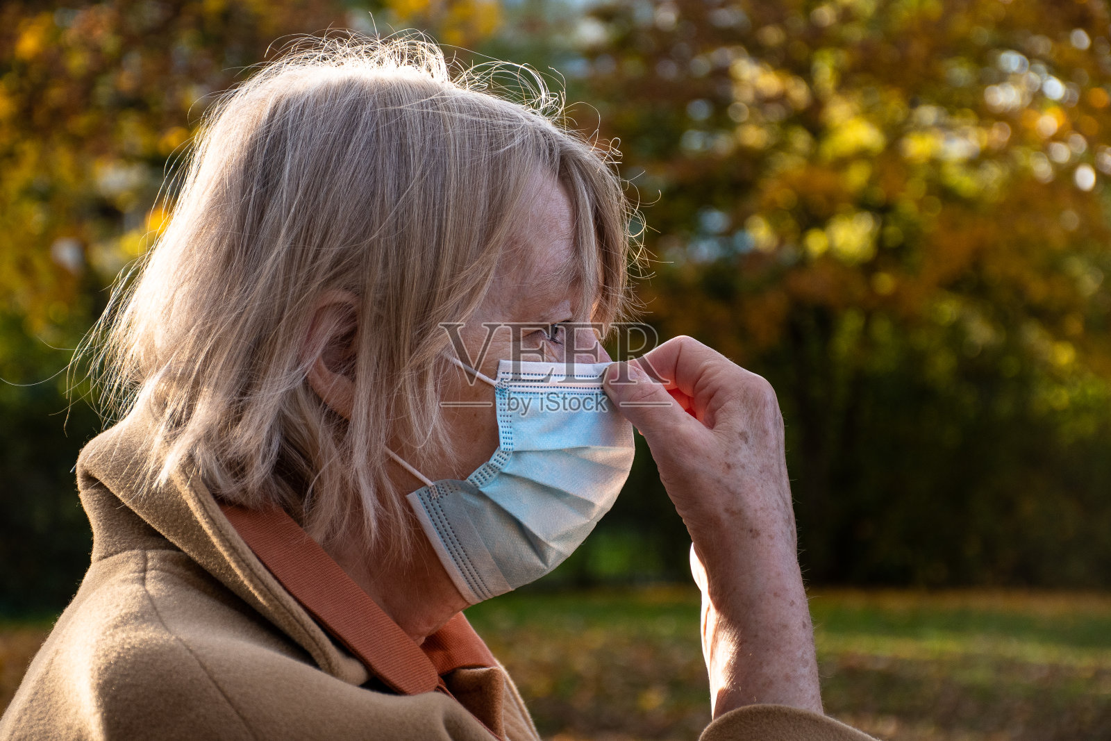 老年妇女在COVID-19大流行期间调整口罩照片摄影图片
