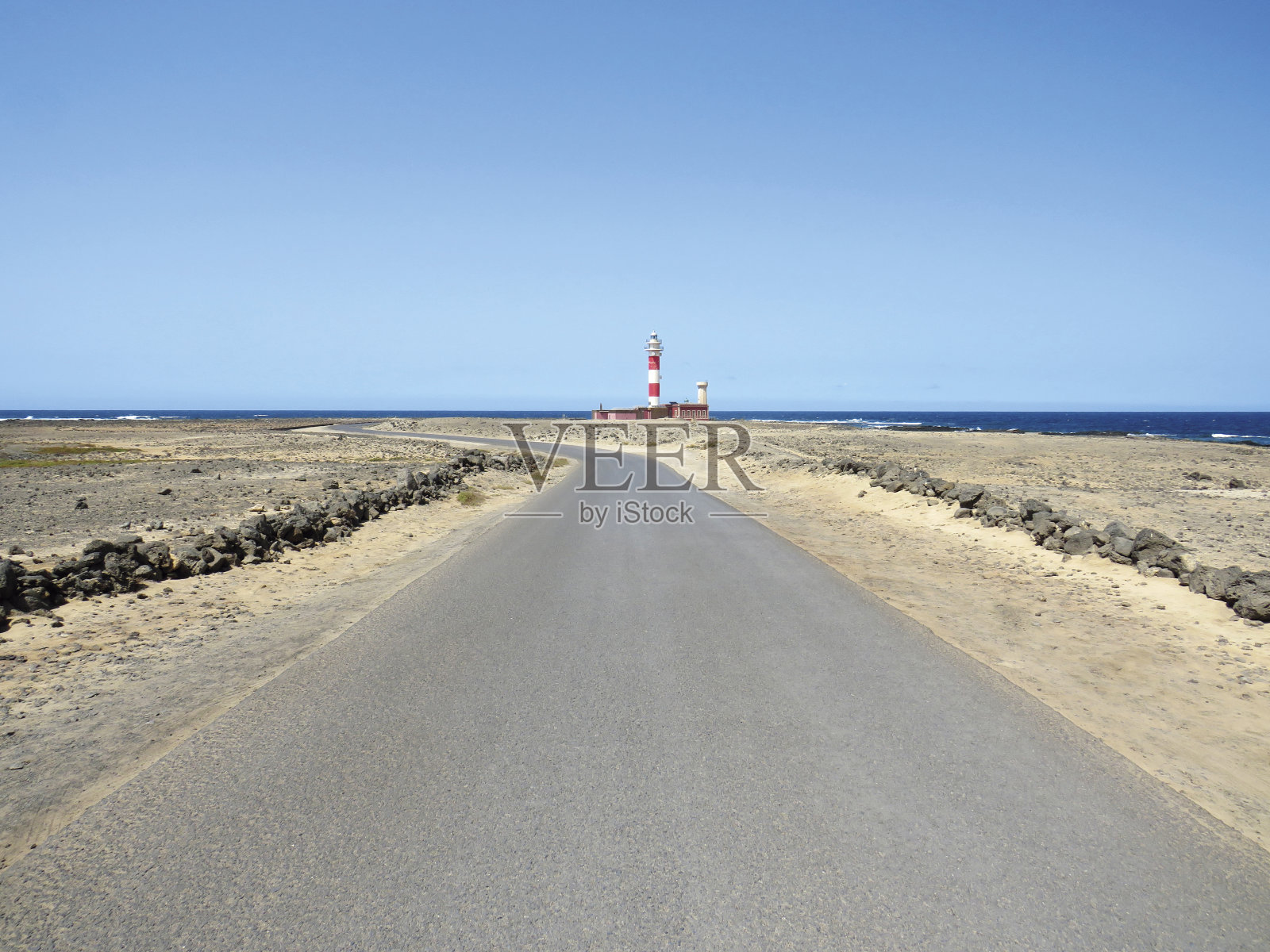 在蓝色的海洋和天空下，通向红白相间的海上灯塔的荒僻道路。疯子的海岸景观。建筑和造船的细节。海上安全背景照片摄影图片