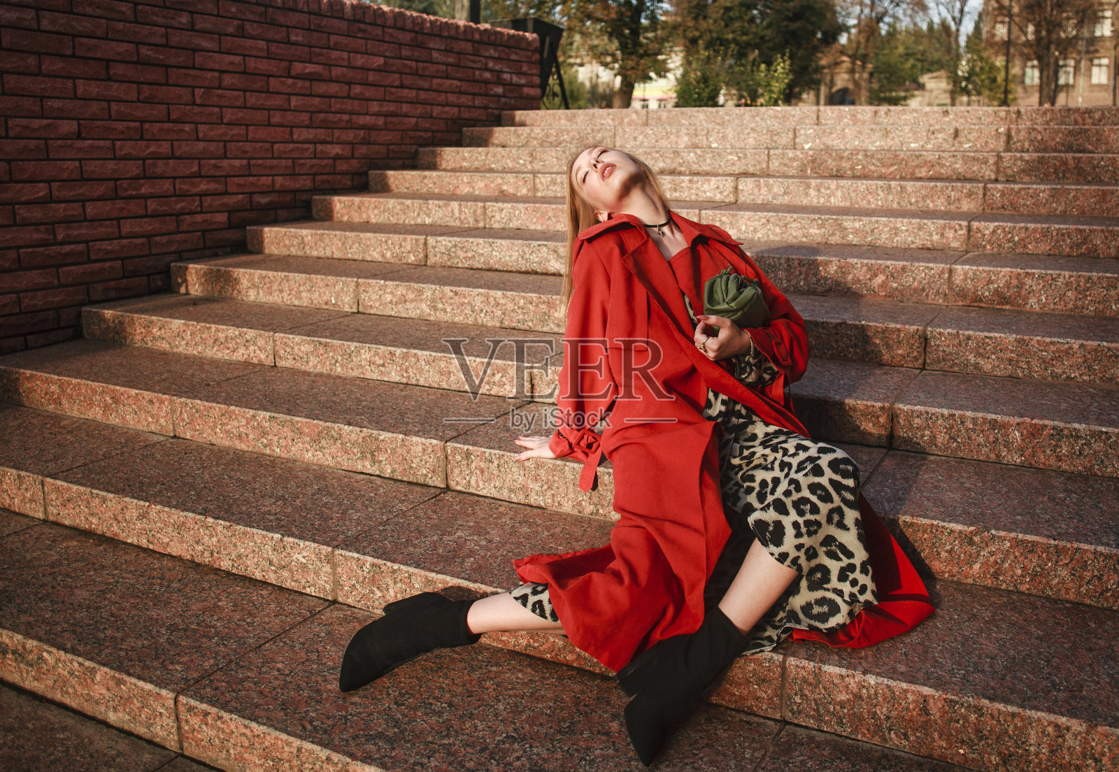 优雅的淑女女孩穿着陶土色的外套，在砖墙背景的城市街道上摆姿势照片摄影图片