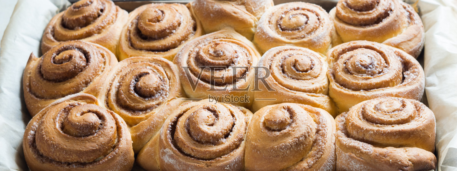 新鲜烘焙的肉桂面包，烤羊皮纸上的肉桂卷。顶视图,特写。甜自制糕点圣诞烘焙。照片摄影图片