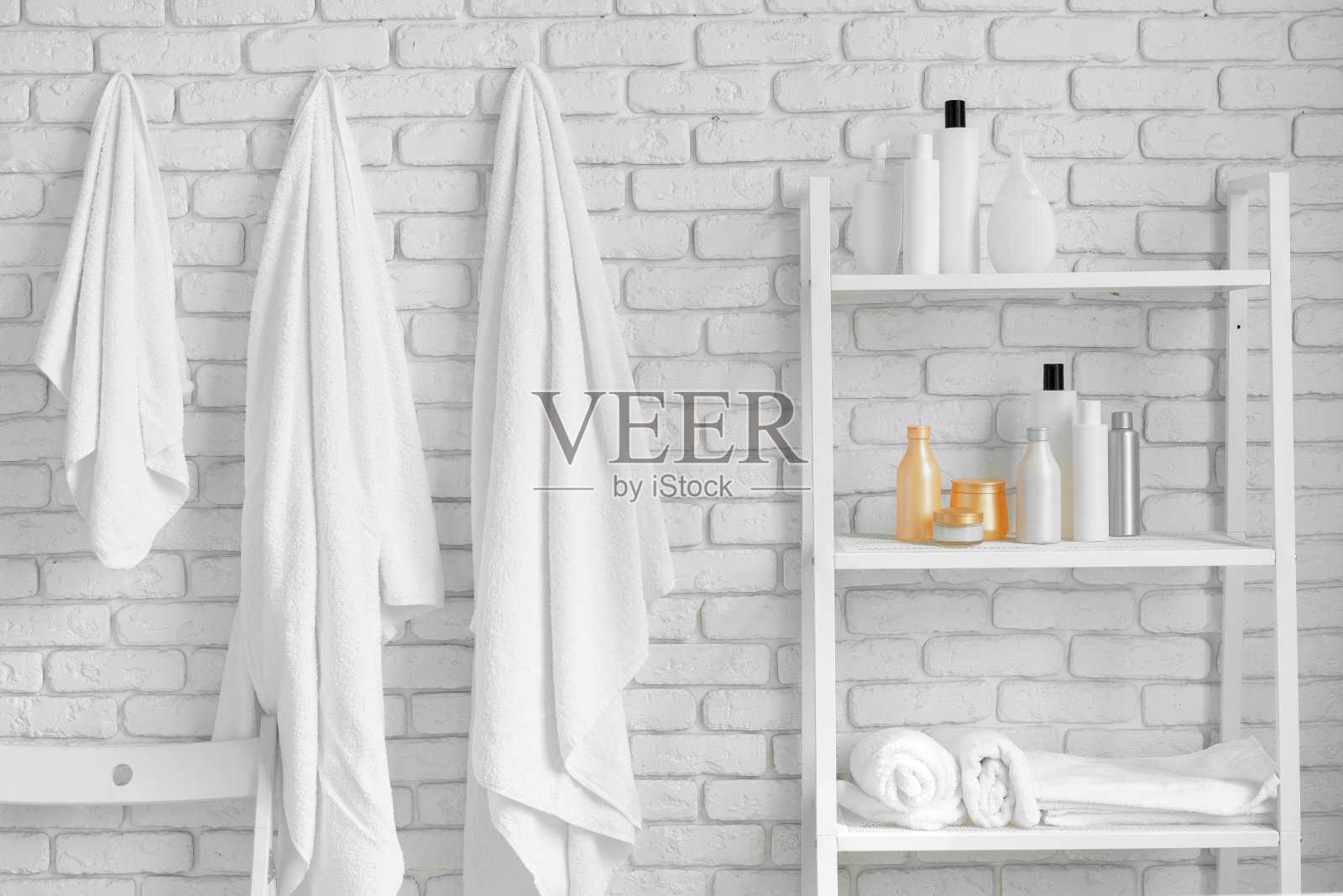 白砖墙边的浴室架子上放着化妆瓶和挂毛巾照片摄影图片