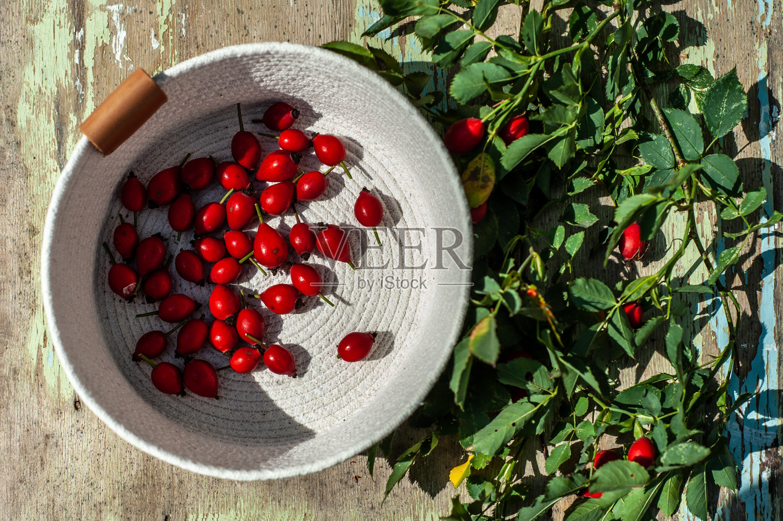 红色的浆果在底部，白色的篮子在破旧的颜色木制表面。狗玫瑰的小枝就在它旁边照片摄影图片
