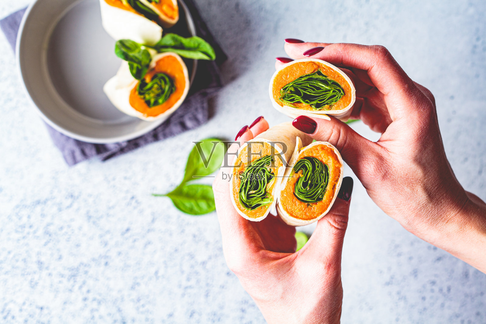 纯素玉米饼卷红薯和菠菜在手，灰色背景，俯视图。健康素食理念。照片摄影图片