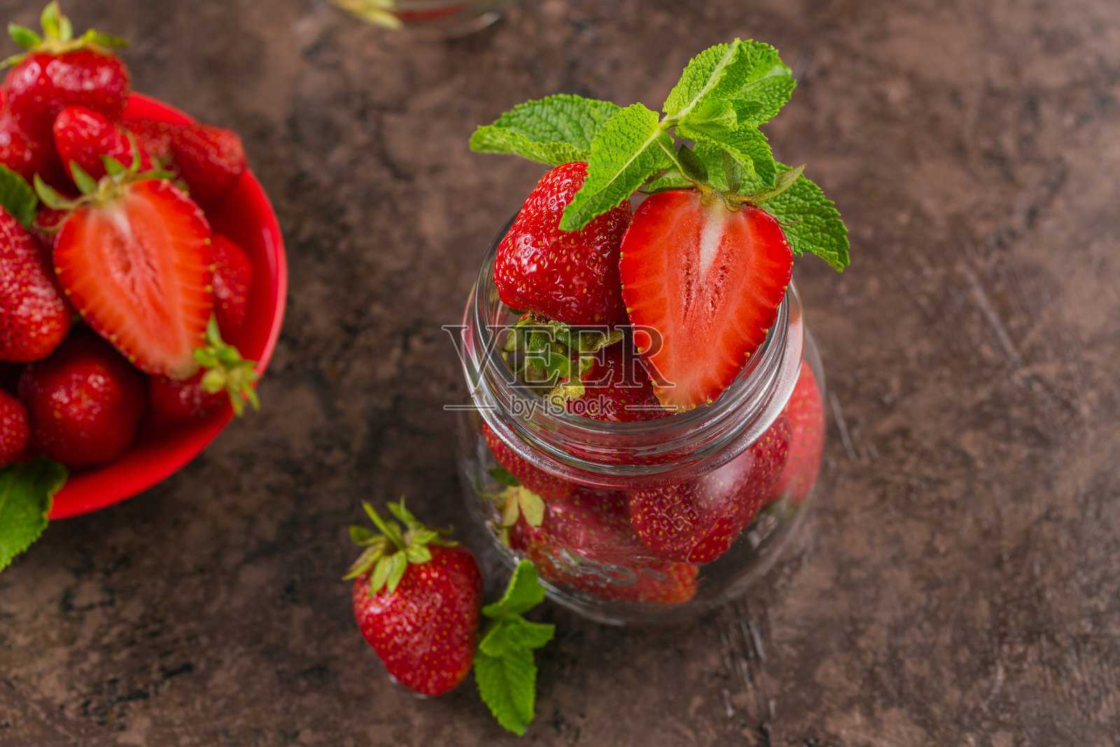 深褐色的桌子上放着一罐红色多汁的草莓。健康饮食的休闲食品理念。照片摄影图片